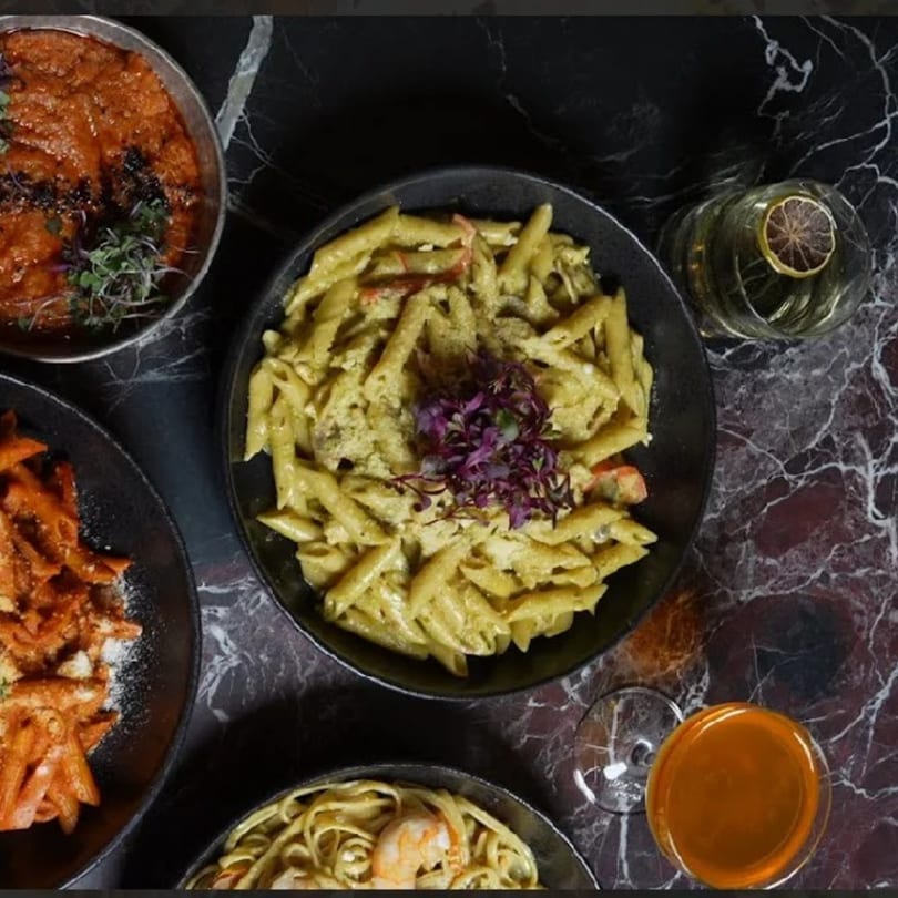 Overhead view of various pasta dishes and drinks on a dark marble table at Adana Restaurant.