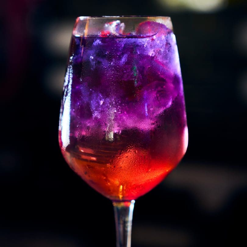 A vibrant purple and red cocktail in a wine glass, with condensation on the glass.